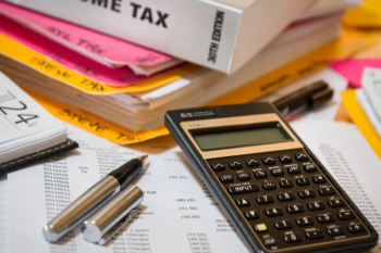 Calculator, pens, and tax documents on a desk during tax preparation.