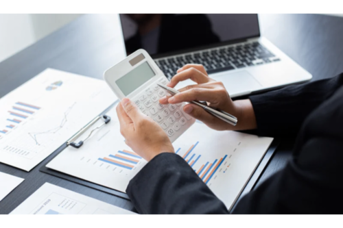 Person using calculator with financial charts and laptop.