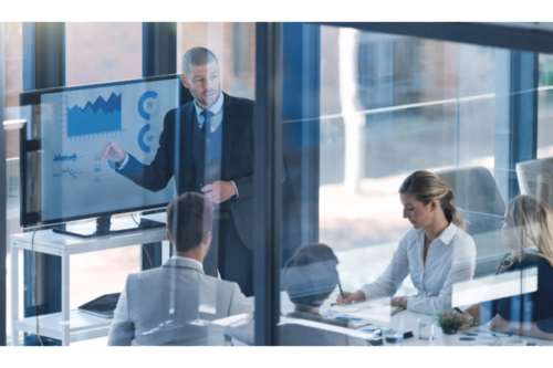 Business team in meeting with presenter showing financial charts.