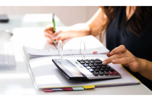 An accountant using calculator and writing in binder at desk.