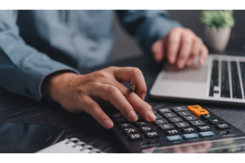 Person using calculator and laptop for tax calculation.